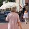 Alte Frau mit Sonnenschirm geht auf einer Straße spazieren.