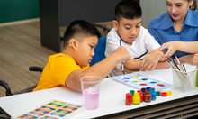 Eingliederungshilfe - zwei Kinder sitzen am Tisch und malen mit Unterstütz