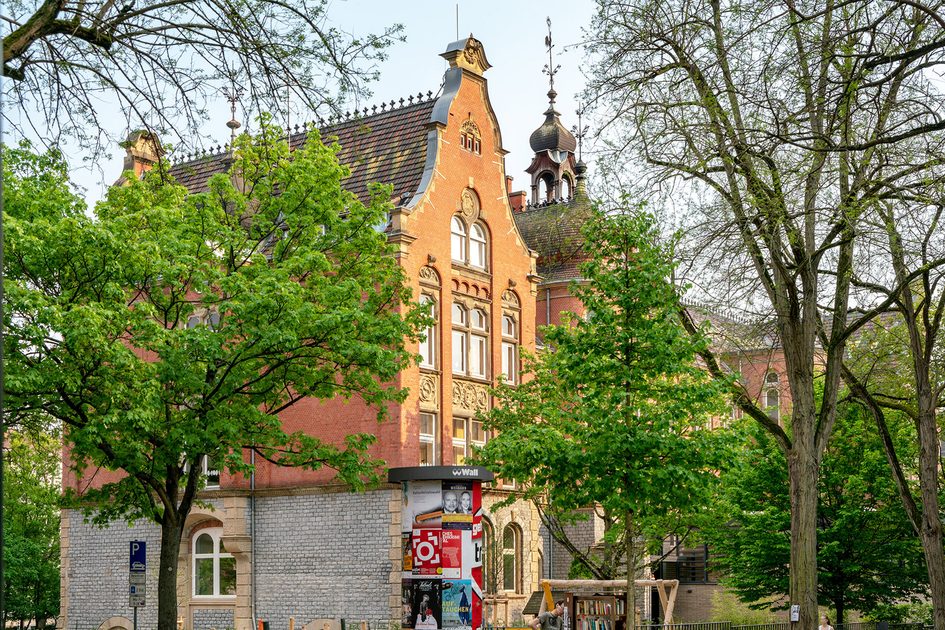 Historischer Gebäude mit Spielplatz vor Grünanlage.