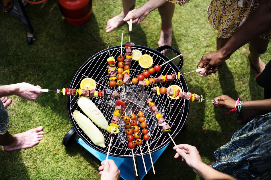 Draufsicht kleiner Kohlegrill mit darüber gehaltenen Grillspießen