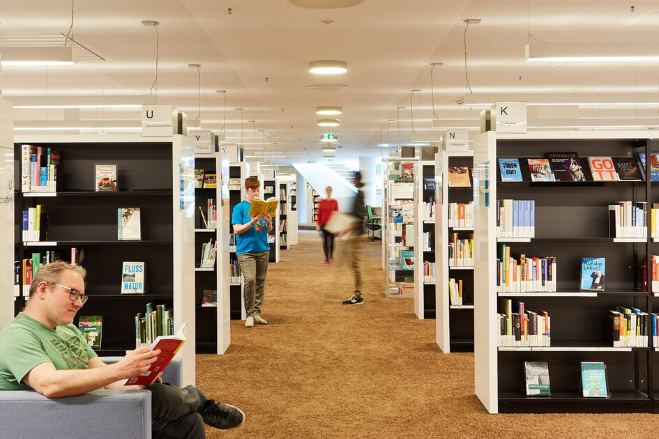 Mehrere Bücherregale und Personen, die in den Texten stöbern.