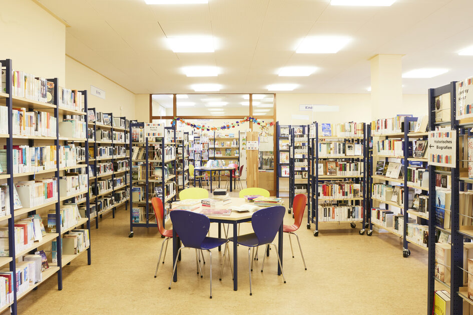 Un tavolo si trova tra alcuni scaffali della biblioteca del quartiere.