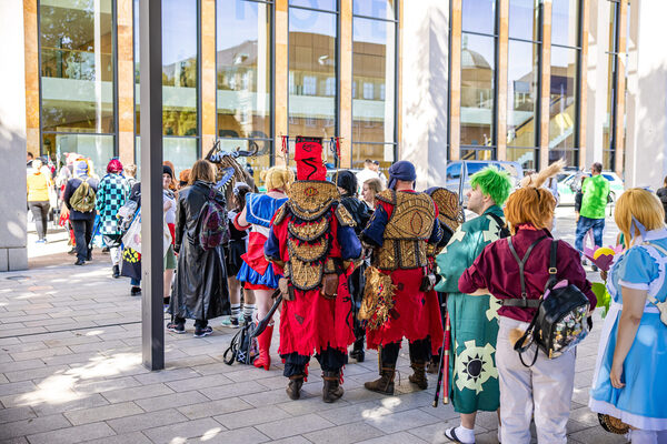Verkleidete Menschen in einer langen Schlange vor einem großen Gebäude.