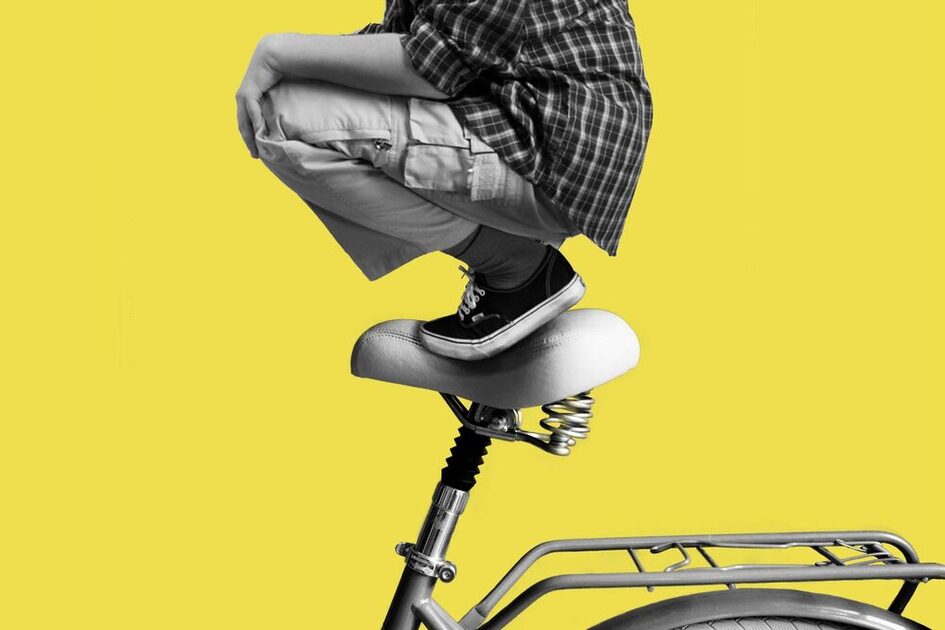 Vor gelbem Hintergrund hockt ein Mensch auf einem weißen Fahradsattel