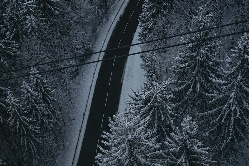 Птичи поглед към път, заобиколен от заснежена гора