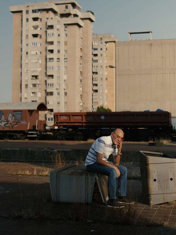 Ein Mann sitzt auf einem Betonklotz vor einem Hochhaus