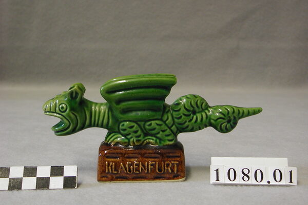Статуетка на зелен дракон, глазирана със сол, върху кафява основа с надпис Klagenfurt