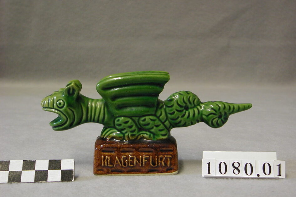 Salzglasierte grüne Drachenfigur auf braunem Sockel mit Aufschrift Klagenfurt