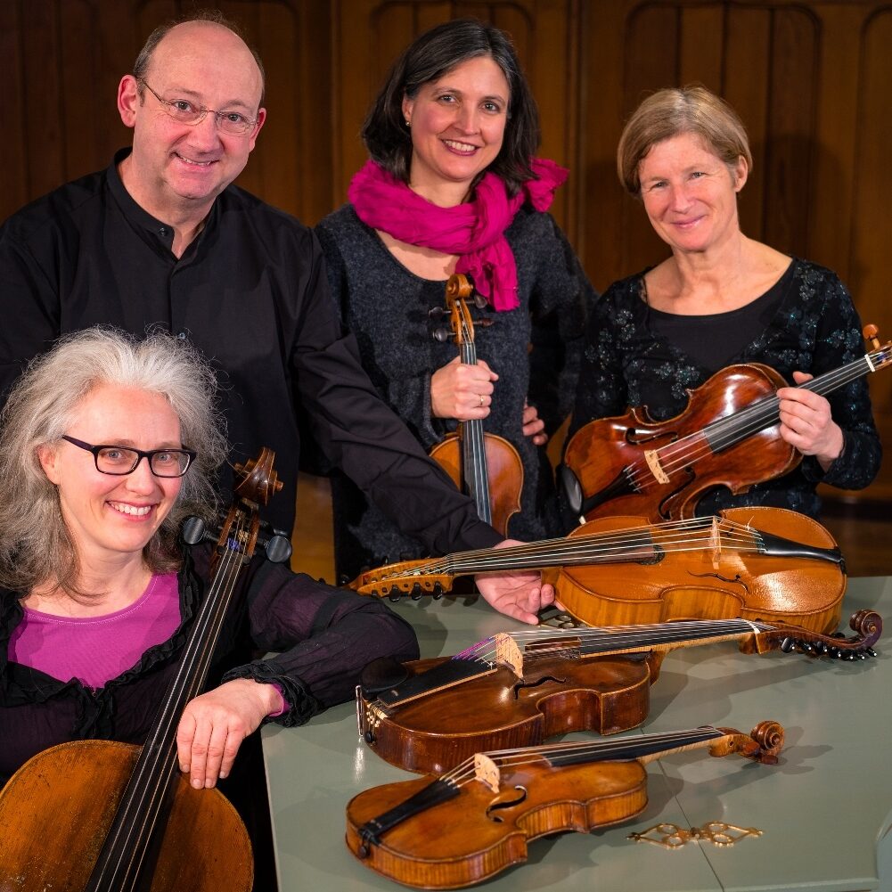 Left front woman with glasses and a baroque violoncello, left back man with glasses and a viola, center back a woman with a baroque violin, right back a woman with a baroque violin.