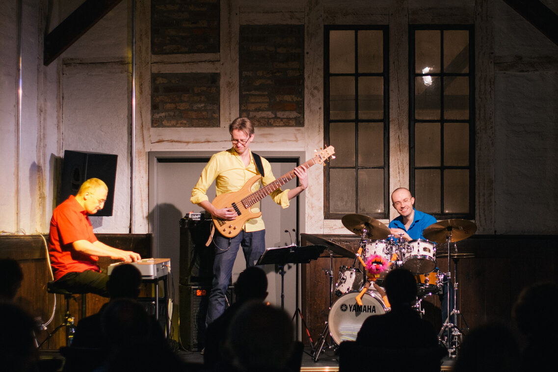 Solda piyanoda bir adam, ortada bas gitar çalan bir adam ve sağda davul çalan bir adam. Eski bir evde bir sahnede çalıyorlar. Herkes gülümsüyor ve eğleniyor. Rengarenk kıyafetler giymişler.
