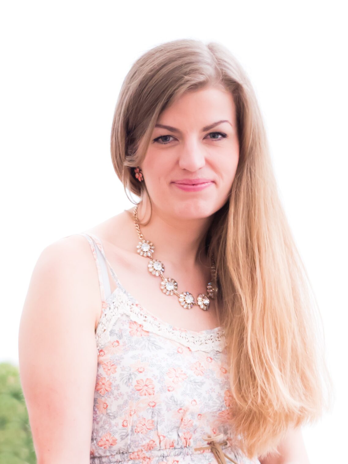 Блондинка у квітчастій сукні та з великим намистом на шиї. Картина в цілому дуже яскрава, і на задньому плані майже нічого не видно. Художниця посміхається в камеру.