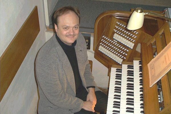Thomas Schermuly sitzt an der Orgel, das Foto ist von oben gemacht und er schaut hoch zur Kamera.