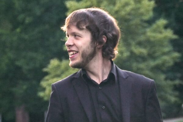 Benjamin Reiter, ein Mann mit braunen Haaren, steht in einem Park und lächelt zur Seite.