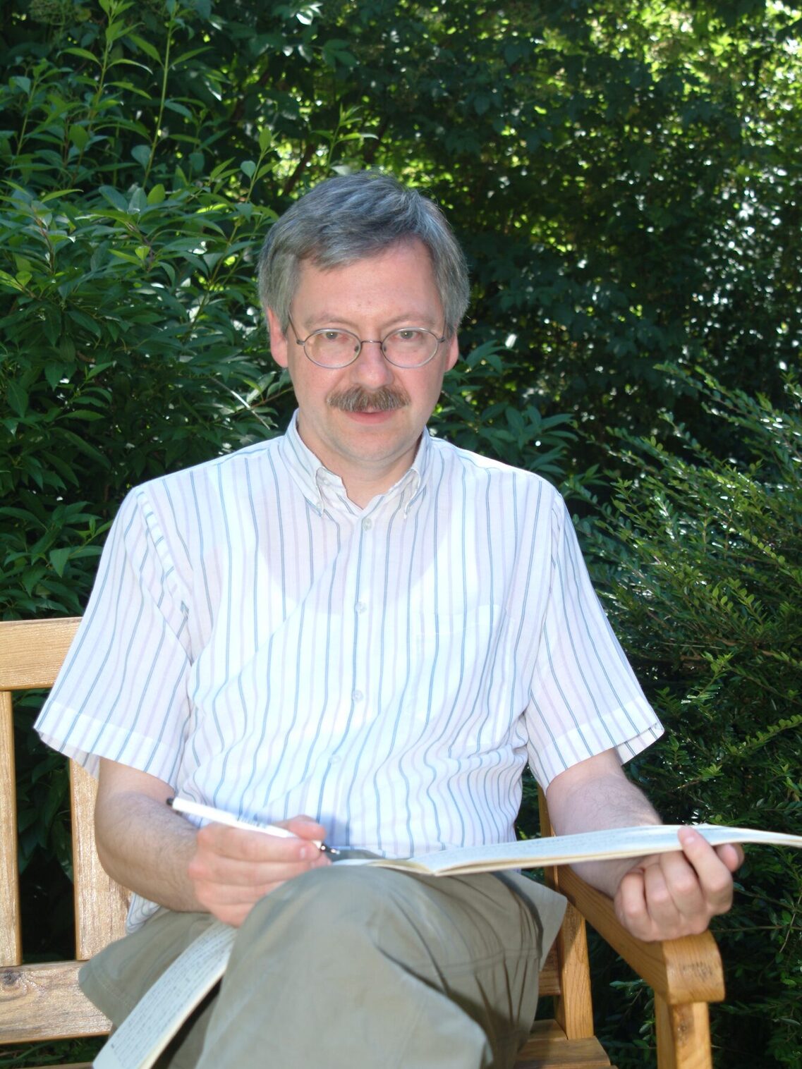 يجلس بوركهارد موهر على مقعد في حديقة وعلى ساقيه دفتر ملاحظات يكتب فيه. ينظر إلى الكاميرا.