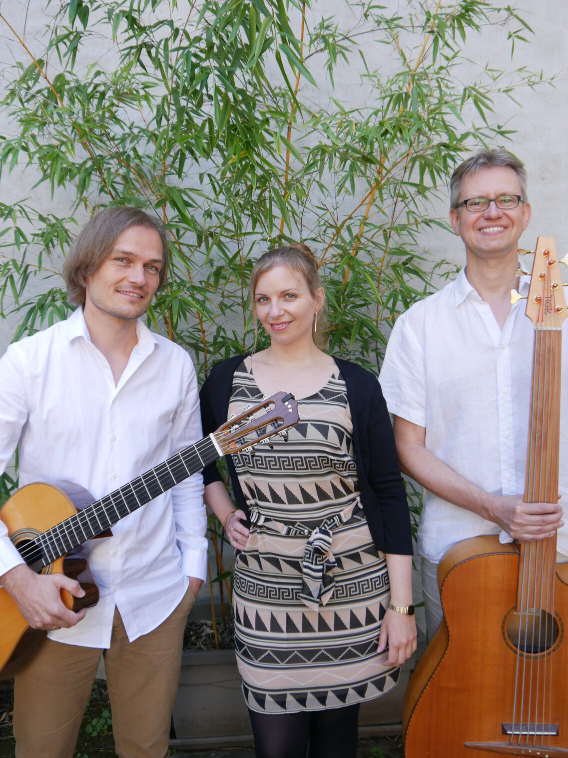 Триото Jazzil застава заедно с инструментите си. Те стоят пред бяла стена и малко дърво. Всички се усмихват в камерата.