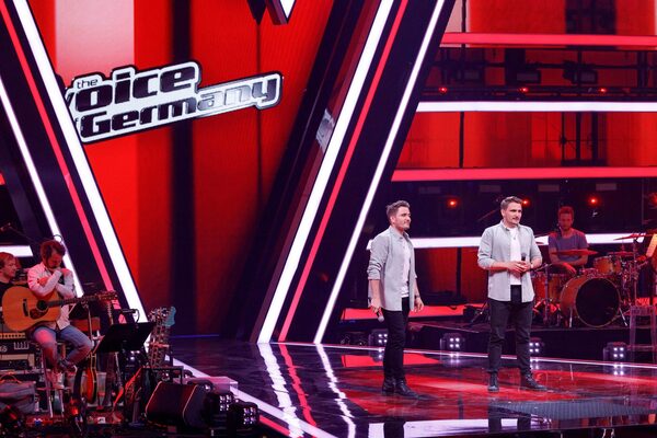 Kingtwiins auf der Bühne von "The Voice of Germany". Alles ist sehr rot und die Zwillinge sehen aufgeregt aus.