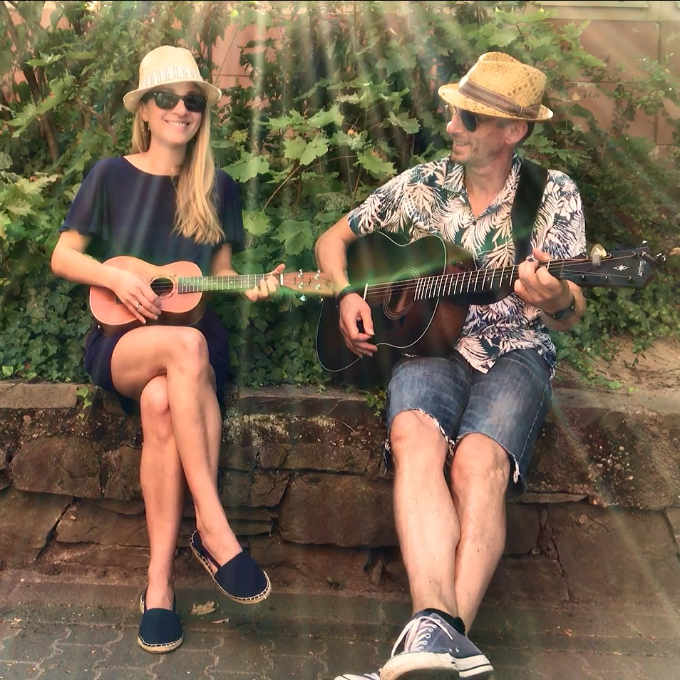 على اليسار امرأة تحمل قيثارة وعلى اليمين رجل يحمل جيتارًا. تخلق أشعة الشمس التي يمكن رؤيتها في الصورة شعوراً صيفياً.