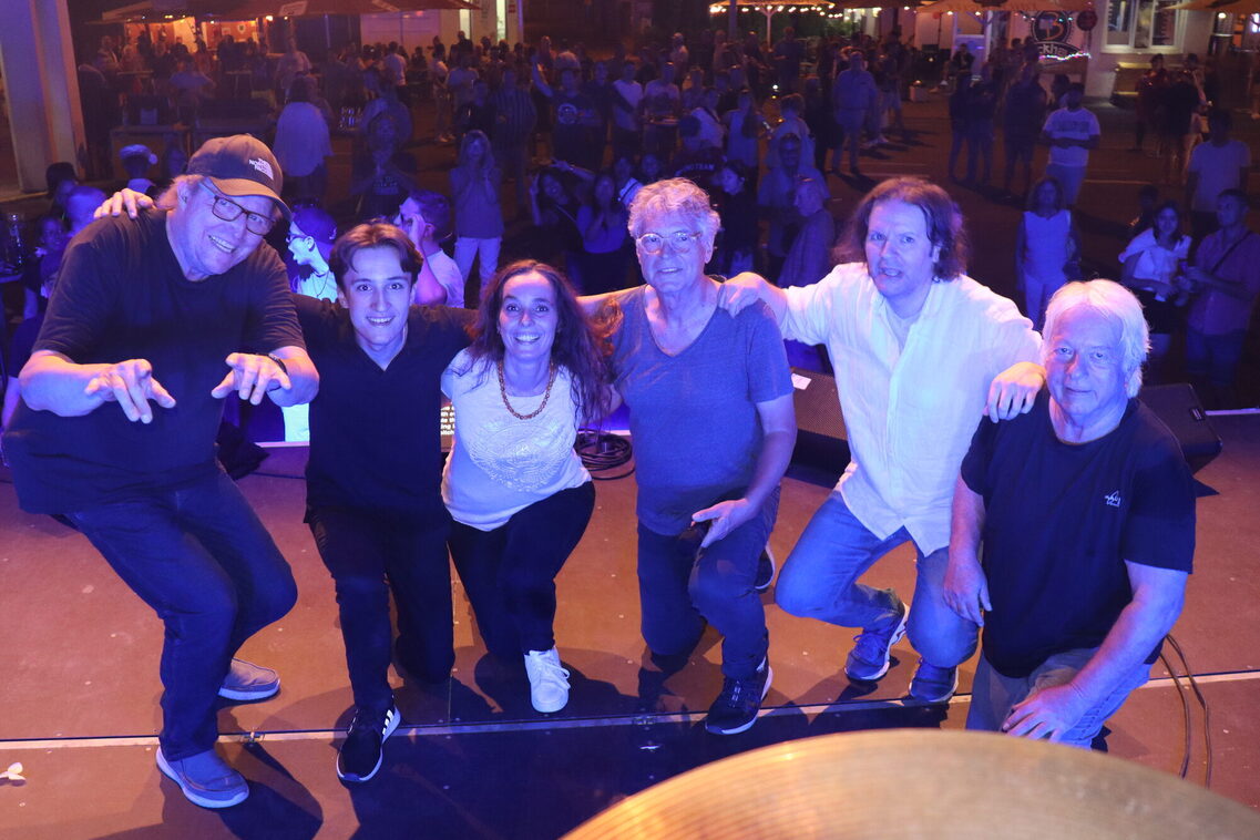 На сцената има петима души (членовете на групата), а на заден план се вижда публиката. Атмосферата е спокойна.