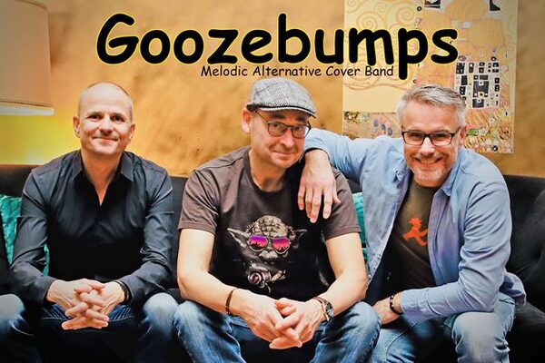 Группа Goozebump сидит на диване и улыбается в камеру. Все три участника выглядят очень расслабленными.