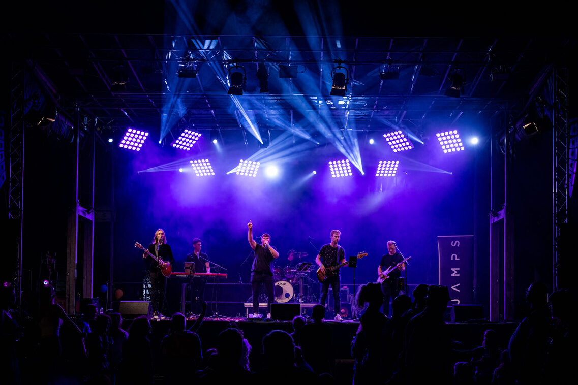 JAMPS pe scena de concert. Pe scenă sunt lumini reci, iar atmosfera este pozitivă.