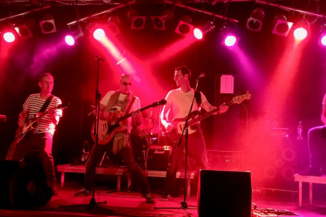 KIES auf Konzertbühne. Es sind viele rote Lichter und die Männer der Band scheinen zu tanzen.