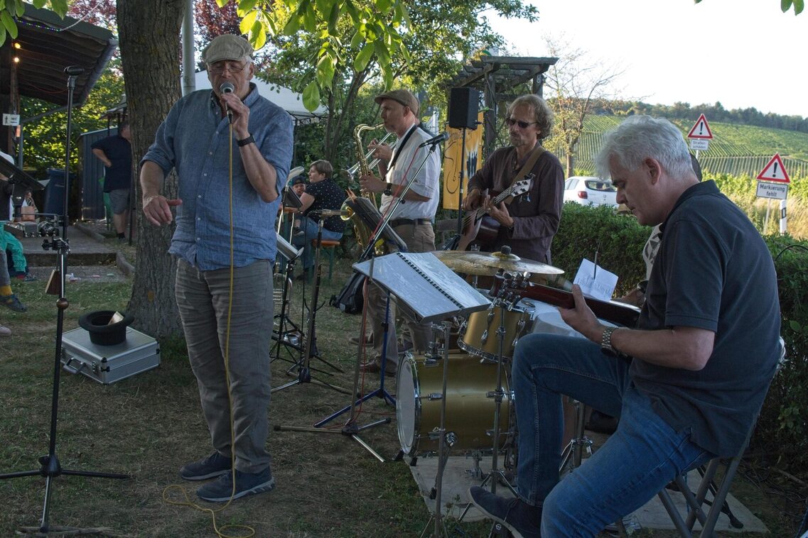 Grup dışarıda bir partide çalıyor. Solda mikrofonda bir adam, arkasında saksafonlu bir adam, onun sağında gitarlı bir adam ve sağ önde elinde bir bas ile davul çalan bir adam.