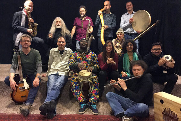 Gruppenfoto von den 12 Mitgliedern mit unterschiedlichen Instrumenten. Alles wirkt etwas chaotisch aber positiv, denn alle haben Spaß.