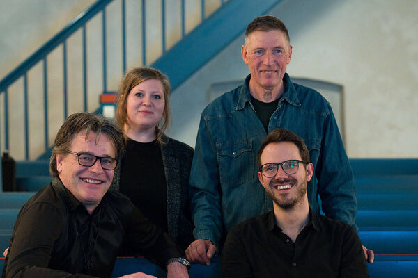 A woman and three men look into the camera.