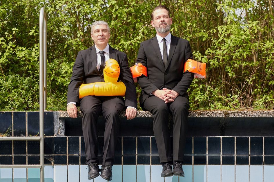 2 Herren am leeren Schwimmbad mit Schwimmflügeln