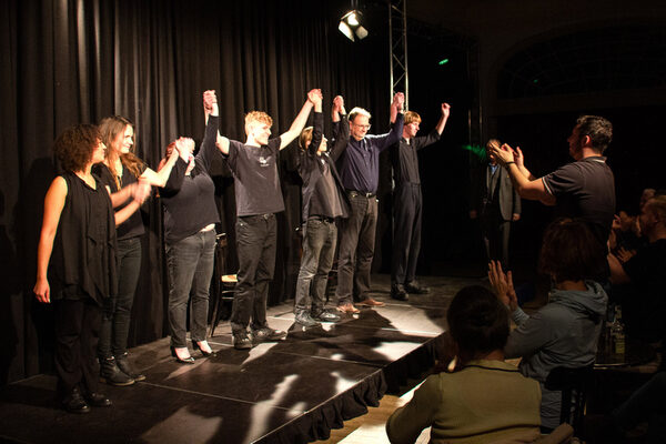 Schauspielerinnen und Schauspieler in schwarzer Kleidung auf einer Bühne.