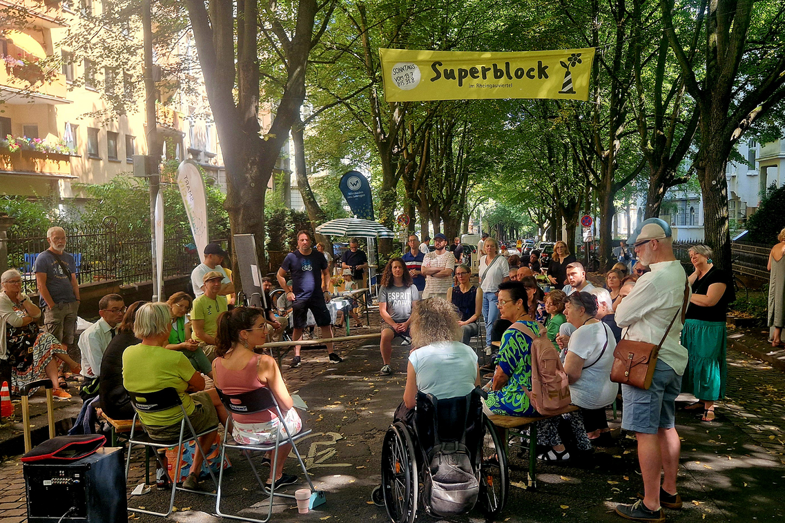 Viele Menschen stehen und sitzen auf einer Straße.