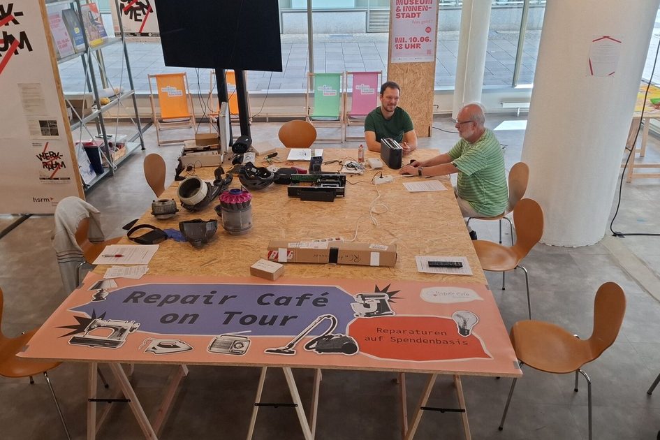 Ein Bild von zwei Männern, die an einem Werktisch sitzen.