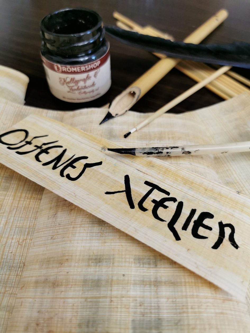 Ein Foto von Schreibutensilien wie Tinte, Papyrus und Schreibfedern.