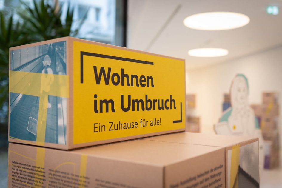Ein Foto von einem Umzugskarton auf dem "Wohnen im Umbruch. Ein Zuhause für alle!" steht.