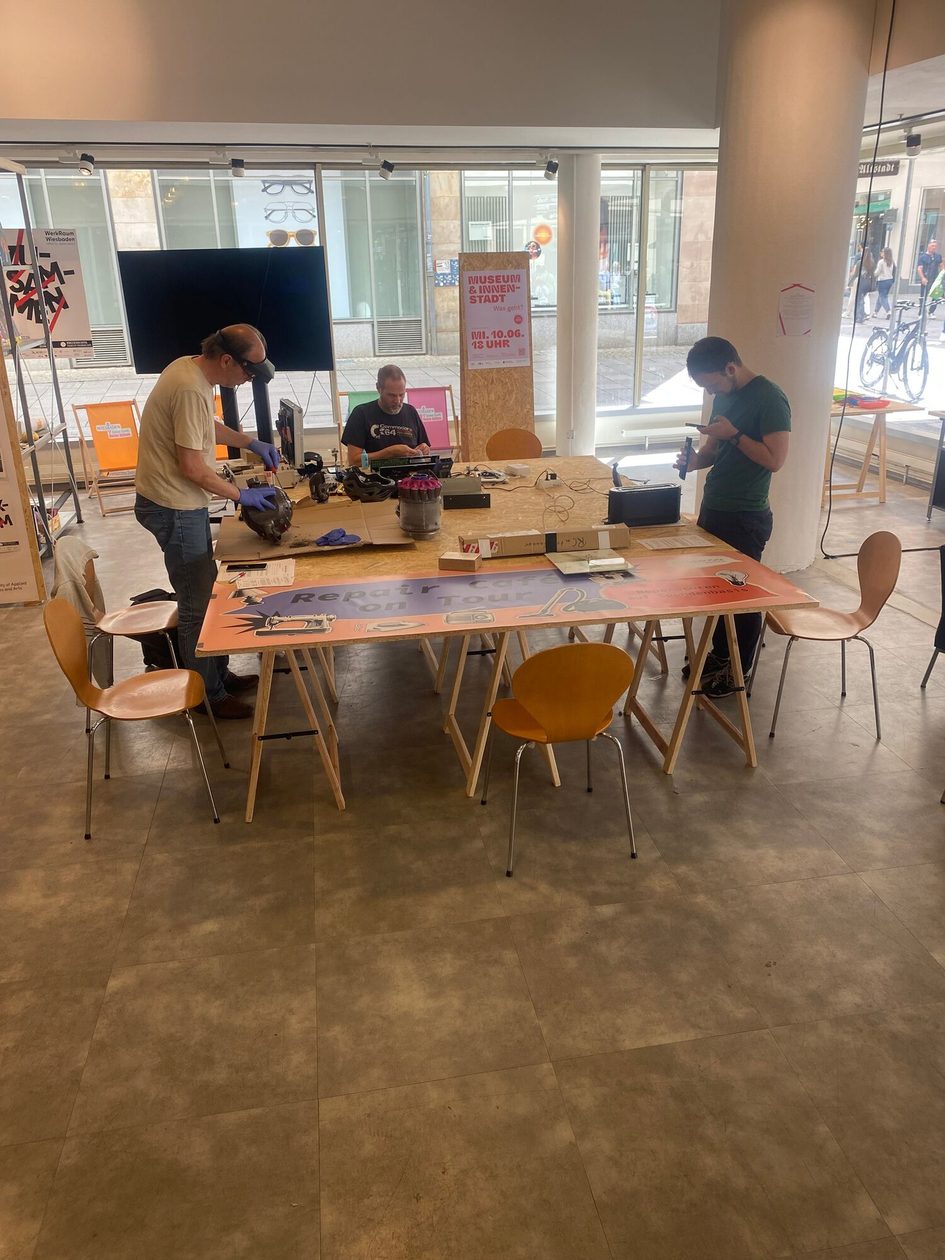 Ein Bild von einem Tisch an dem Menschen etwas reparieren.