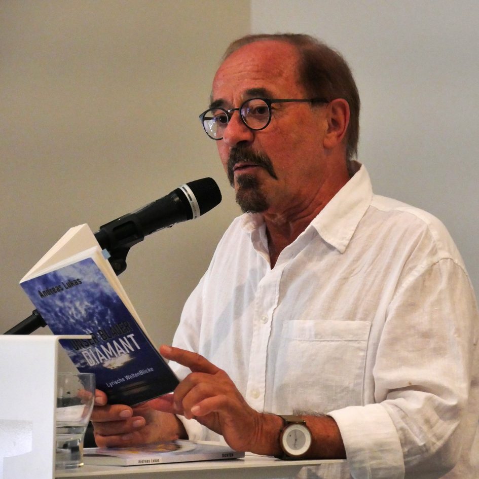 Снимка на мъж, който държи книга в ръка и чете пред публика.