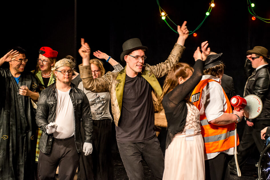 Eine Theatergruppe in bunten Kostümen spielt eine Szene.