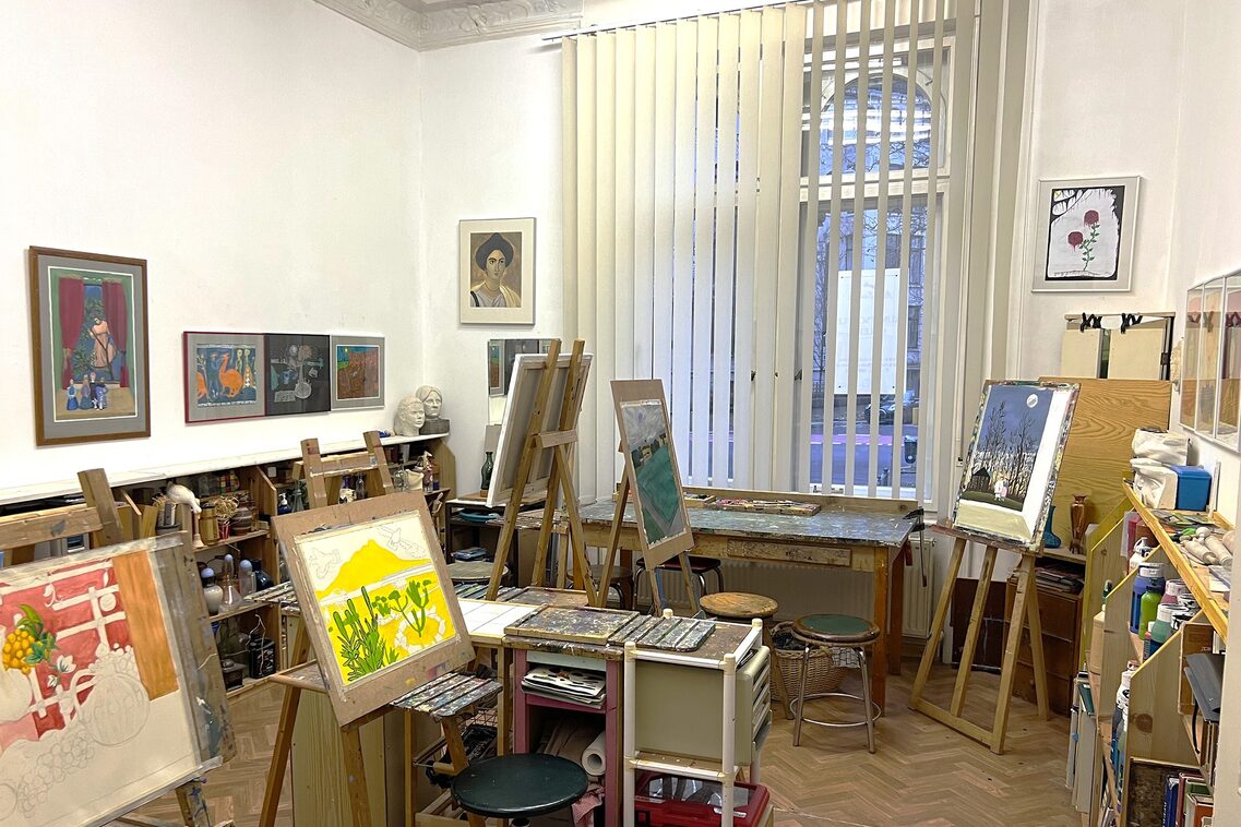 Künstleratelier mit Staffeleien mit Bildern, Tisch und Hockern, Bildern an der Wand