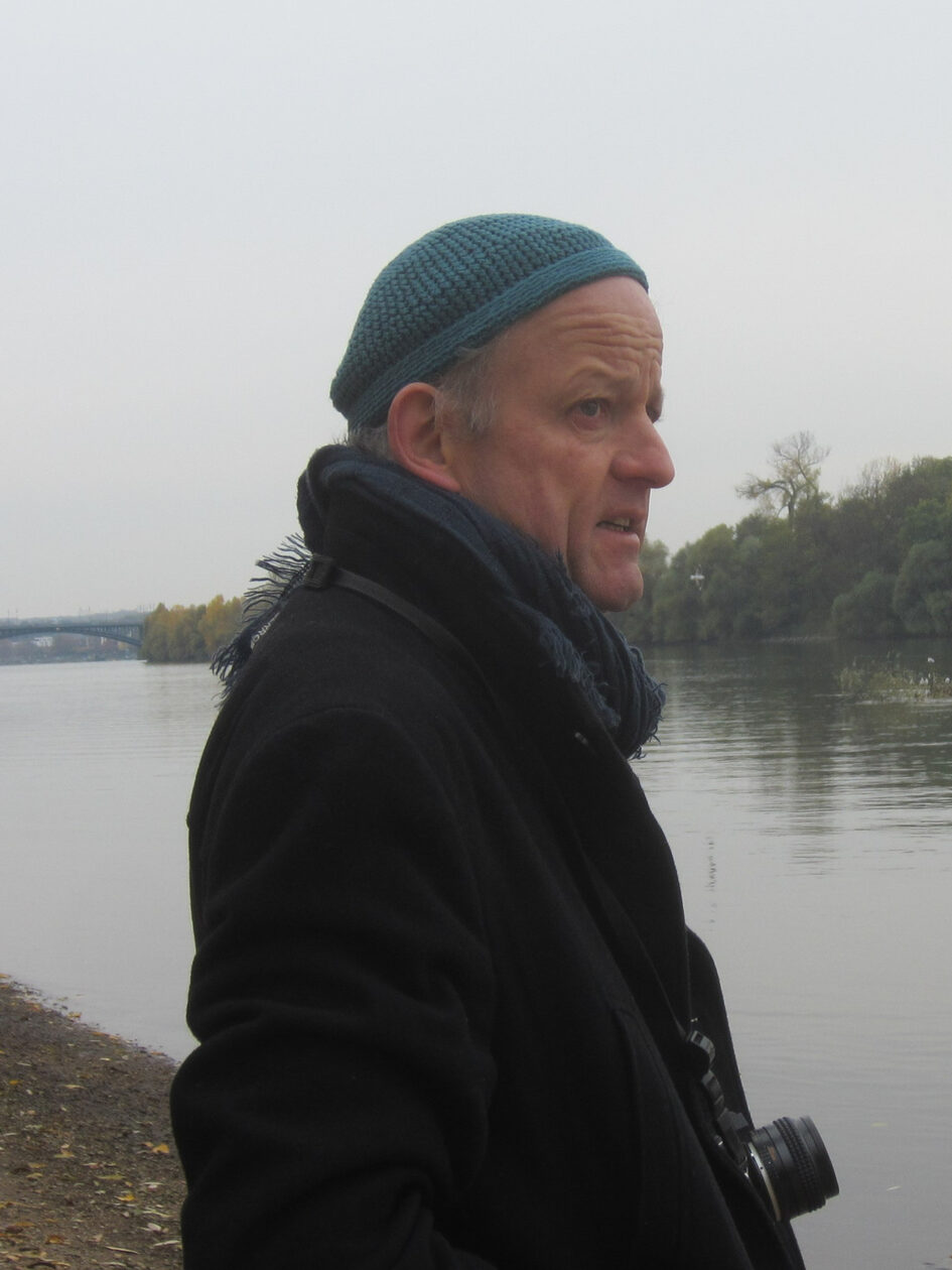 Titus Grab steht mit einer Fotokamera an einem Gewässer.