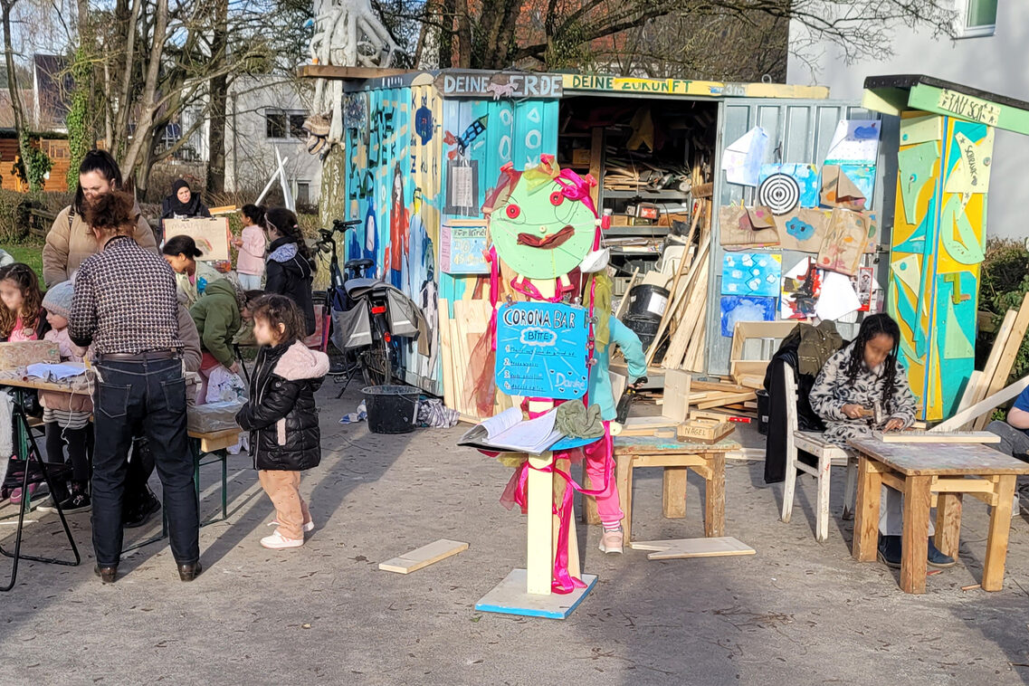 Kinder und Erwachse vor einem bunten Baucontainer mit bunten Collagen und Skulpturen