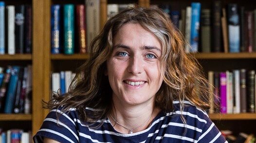 Mujer sonriente con camiseta de rayas delante de una pared de libros