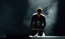 Mann kniet auf der Bühne und wird von einer Lichtquelle angeleuchtet.