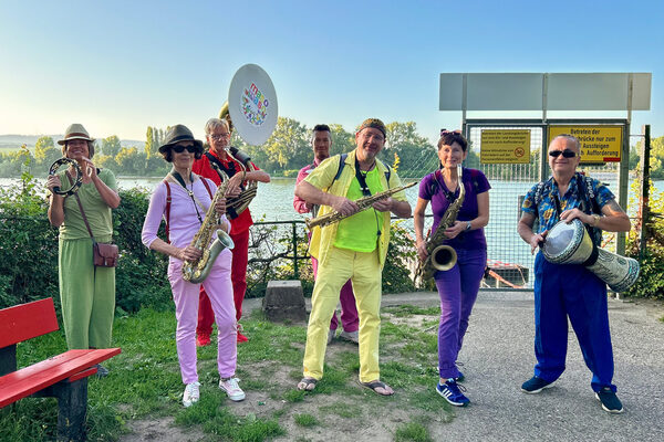 Sieben bunt gekleidete Musiker-innen mit Instrumenten