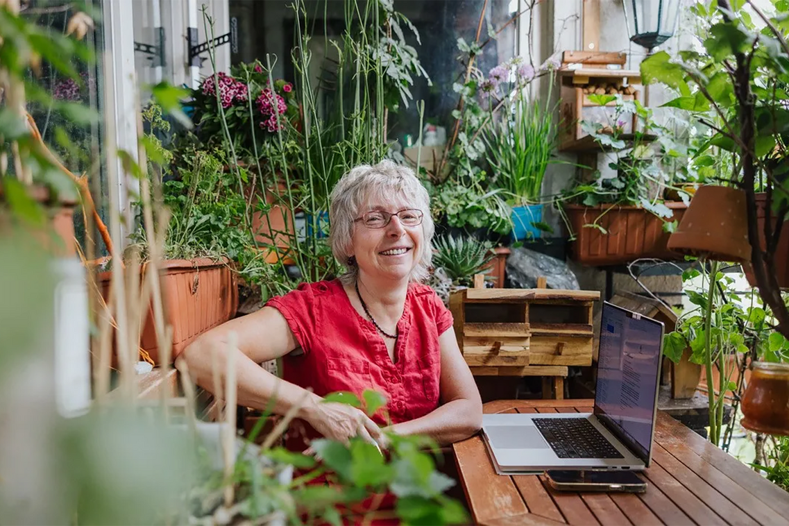 Gärtnern auf kleinsten Raum - Frau sitzt mit Laptop am Gartentisch