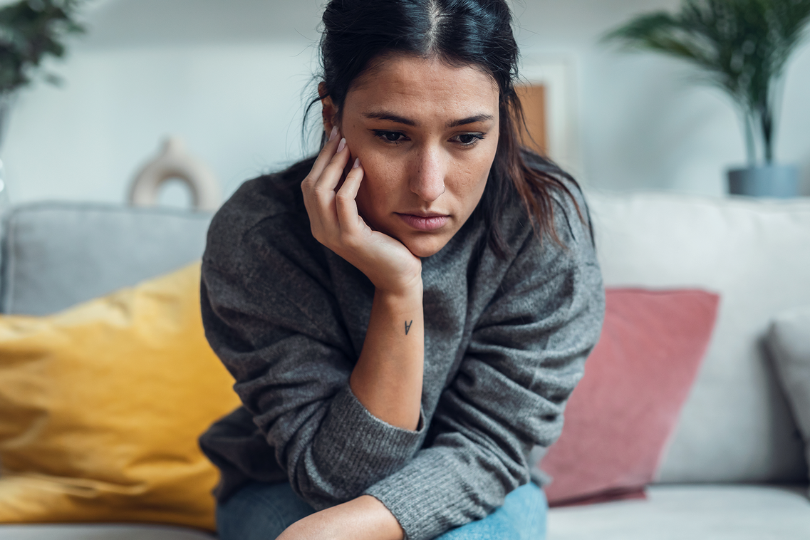 Junge Frau sitzt allein auf dem Sofa.