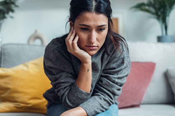 Junge Frau sitzt allein auf dem Sofa.