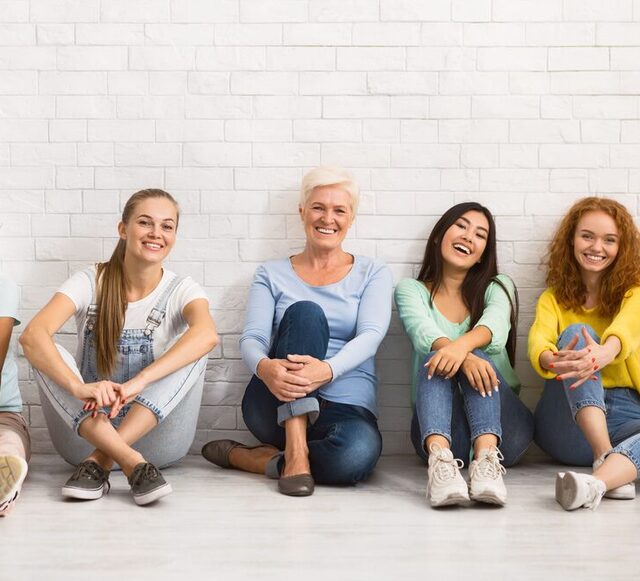 Signore di età diverse che sorridono seduti insieme sul pavimento al coperto