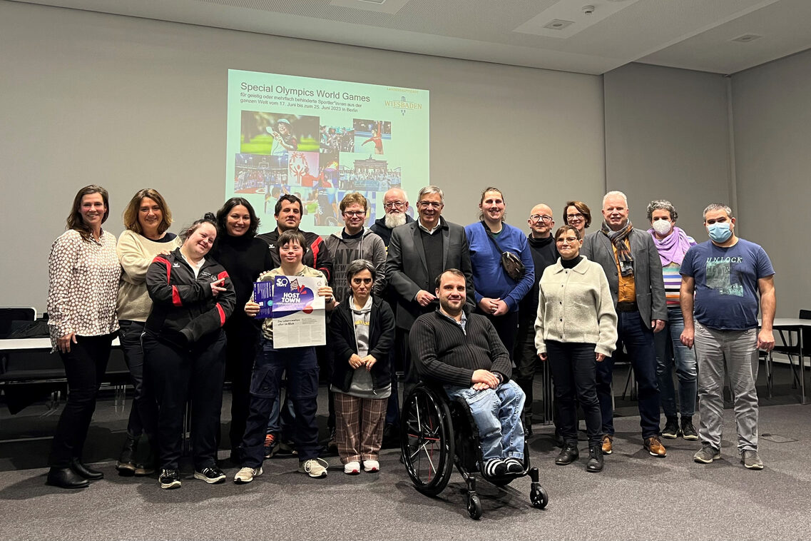 Verschiedene Menschen stehen in einer Gruppe zusammen. Es Rollstuhlfahrer ist Teil der Gruppe.