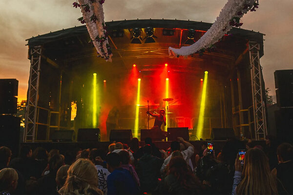 Eine beleuchtete Bühne in der Dämmerung, darauf steht ein Musiker, davor stehen Jugendliche.