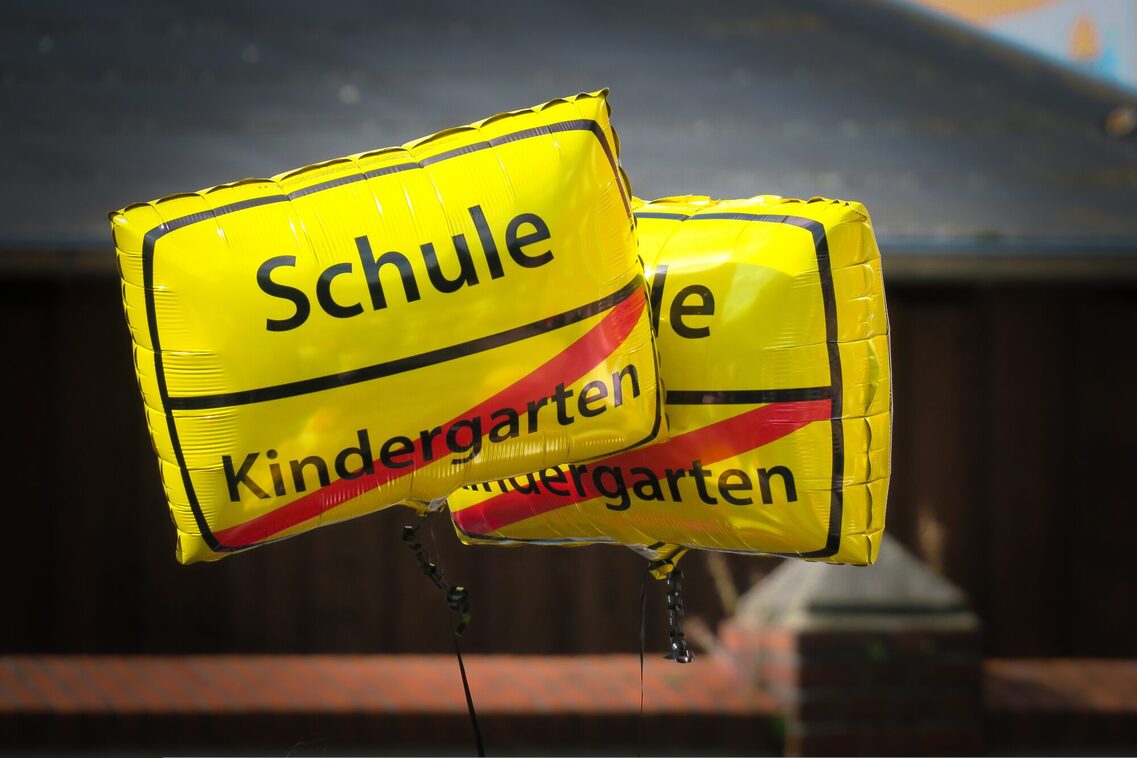 Luftballoons mit der Aufschrift Schule und Kindergarten. Dabei ist das Wort Kindergarten durchgestrichen